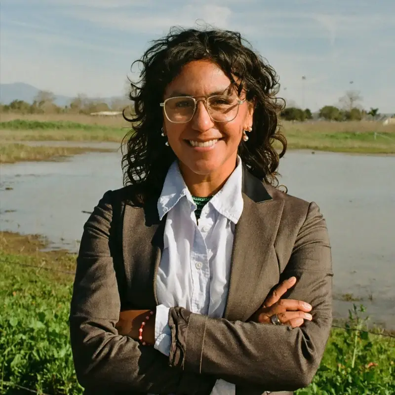 Angely Andrade Vallarta, smiling with arms crossed, in front of a wetland.