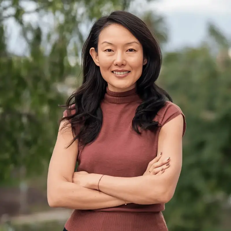 Jane Kim smiling with her arms crossed in front out of focus greenery.