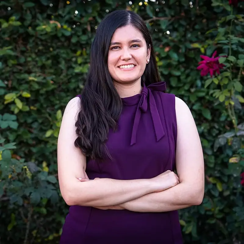 Jessica Guerrero, smiling with arms crossed, in front of greenery.
