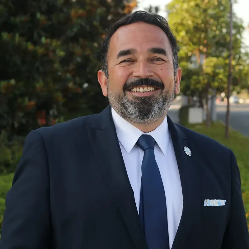 Benjamin Vazquez smiling, wearing a suit, in front of greenery and trees.