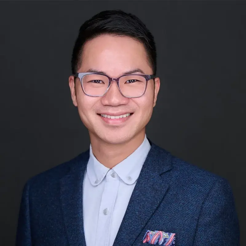 Hieu Nguyen, smiling, wearing a suit in front of a gray background.