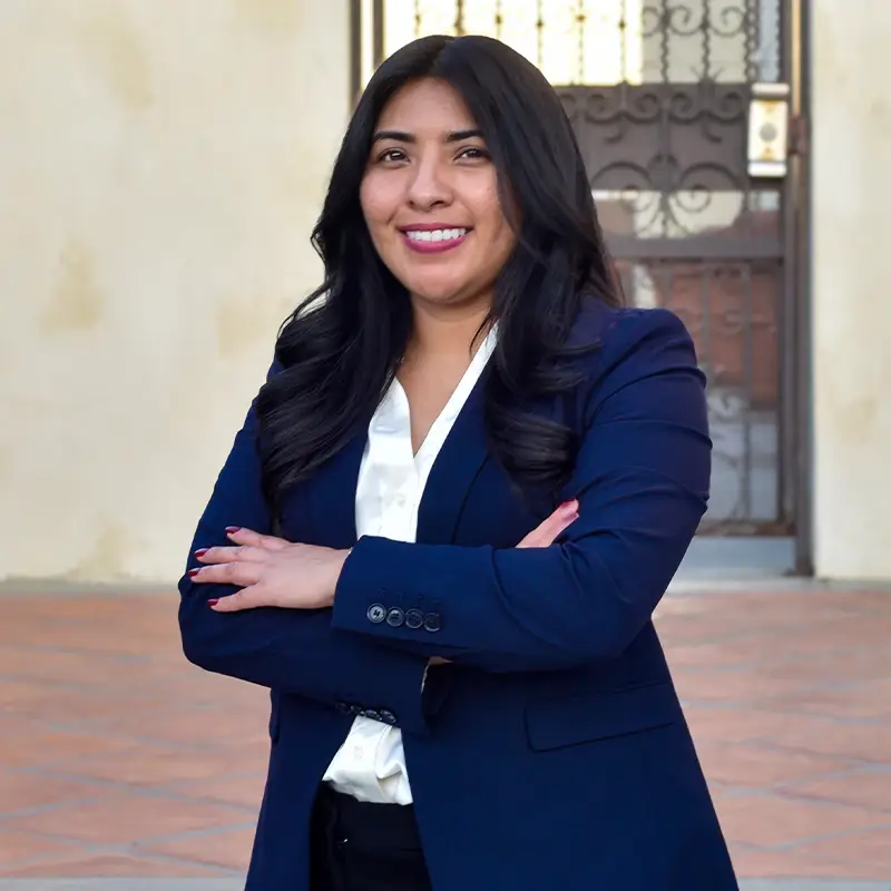 Isuri Ramos, smiling with her arms crossed, in front of a building.
