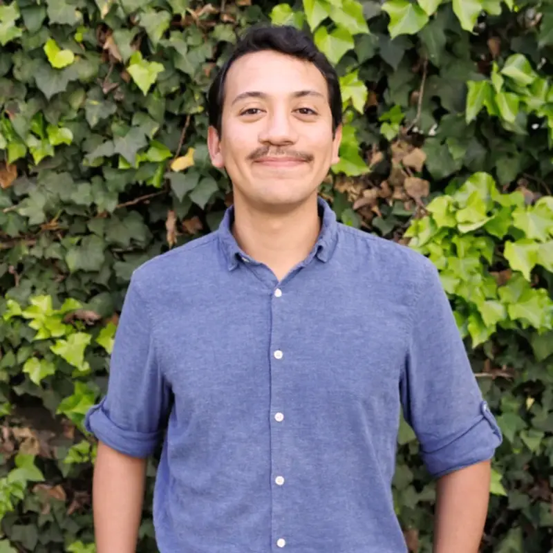 Jozef Maldonado smiling in front of a wall of green ivy.