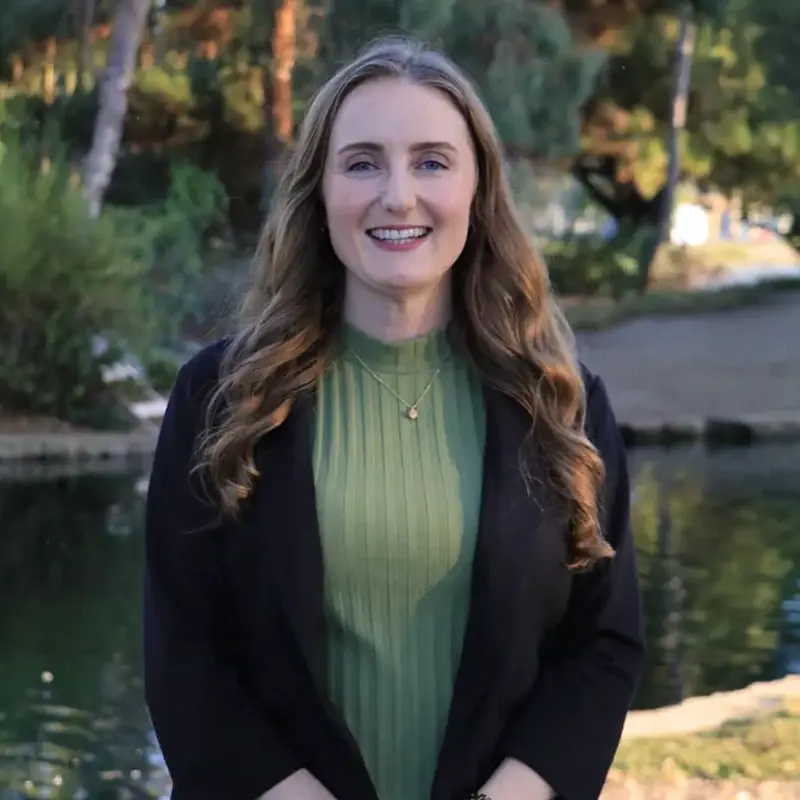 Katelyn Brazer Aceves smiling in front of greenery and a pond.
