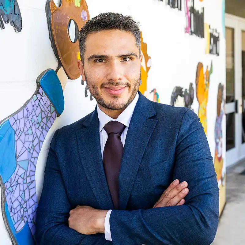 Miguel Alvarez, posing with his arms crossed in front of a colorful mosaic wall.