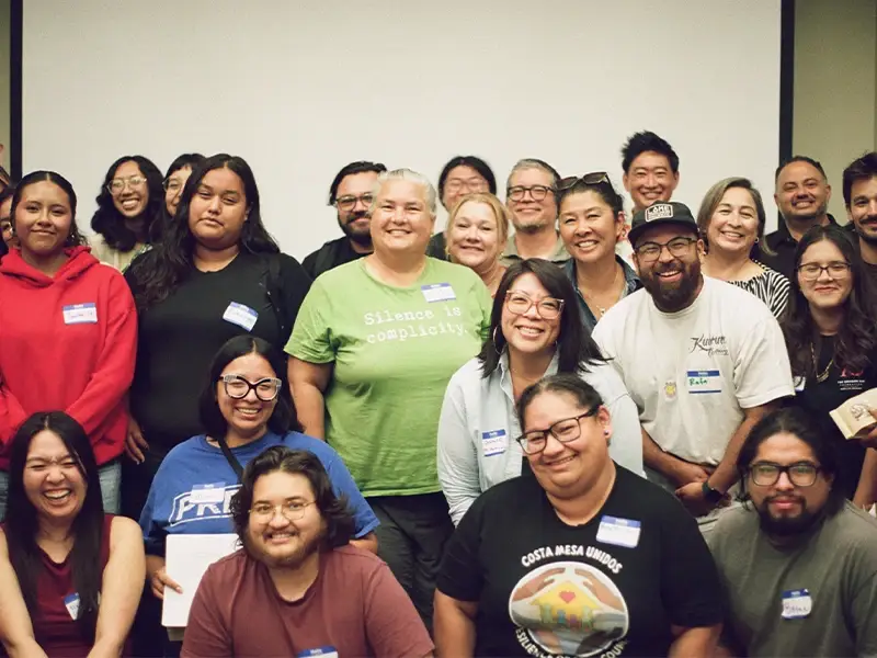 A diverse group of people, arranged in tiers, smiling